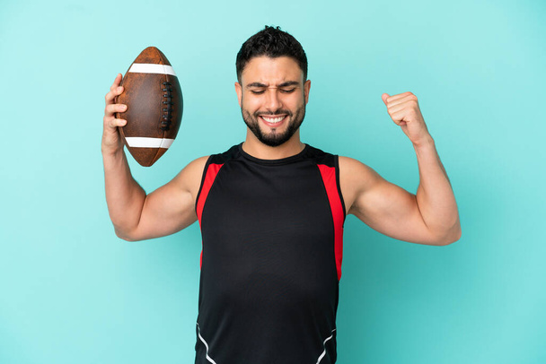 Young arab man playing rugby isolated on blue background doing strong gesture - Foto, afbeelding