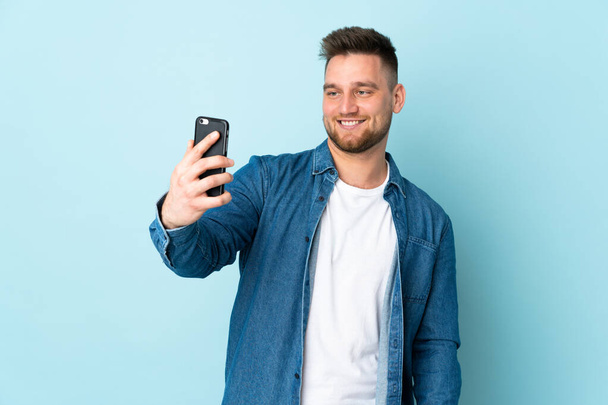 Russe bel homme isolé sur fond bleu faire un selfie - Photo, image