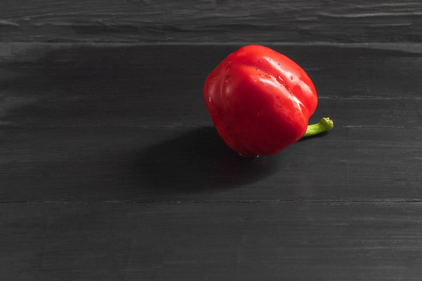 The photo shows an image of a healthy and ripe vegetable. This is red bell pepper. Whole pepper, one on a black background. The pepper glistens from the water left on it after washing - Foto, Imagen