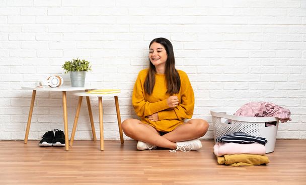 Young woman sitting on the floor at indoors with clothes basket smiling a lot - Photo, Image