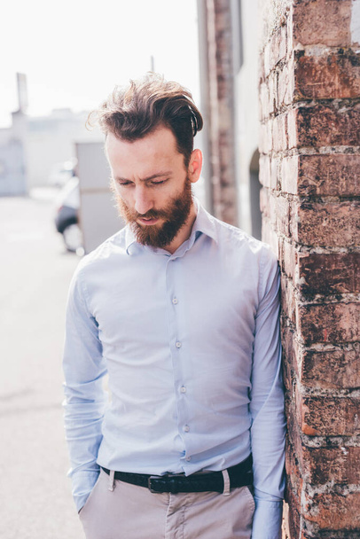 Young bearded man outdoor leaning brick wall looking away pensive  - 写真・画像