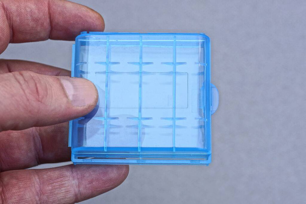 dita a portata di mano tengono blu scatola di plastica chiusa su sfondo grigio - Foto, immagini