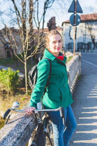 young woman outdoor with bicycle leaning looking camera - Photo, Image