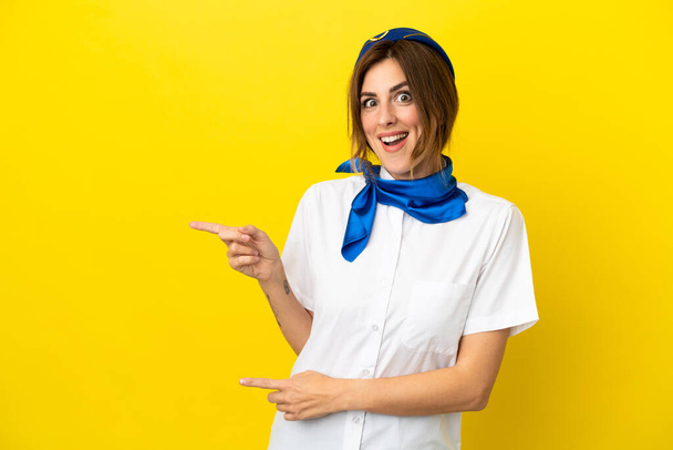 Airplane stewardess woman isolated on yellow background surprised and pointing side - Photo, Image