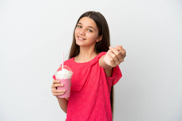 Маленька дівчинка з полуничним молочним коктейлем над ізольованим білим тлом, що заробляє гроші жестом
 - Фото, зображення