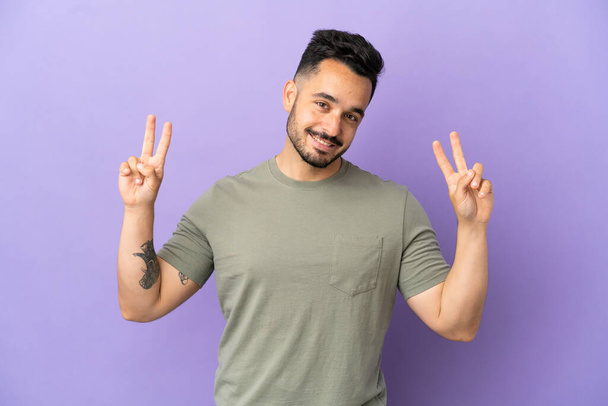 Young caucasian man isolated on purple background showing victory sign with both hands - Photo, Image
