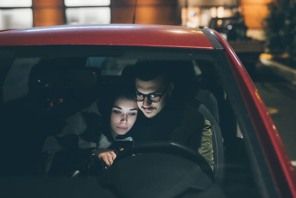 Νεαρό ζευγάρι κάθεται αυτοκίνητο βλέποντας streaming βίντεο στον υπολογιστή τη νύχτα ή online ψώνια ecommerce - Φωτογραφία, εικόνα