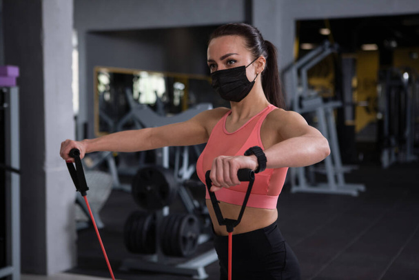 Sportswoman wearing medical face mask, working out at gym during pandemic - Photo, Image