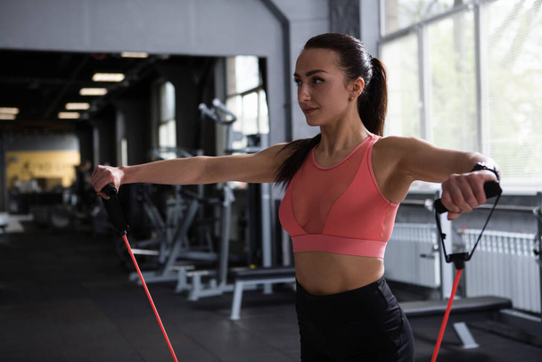 Female bodybuilder warming up shoulders with resistance band before working out at gym, copy space - Photo, Image