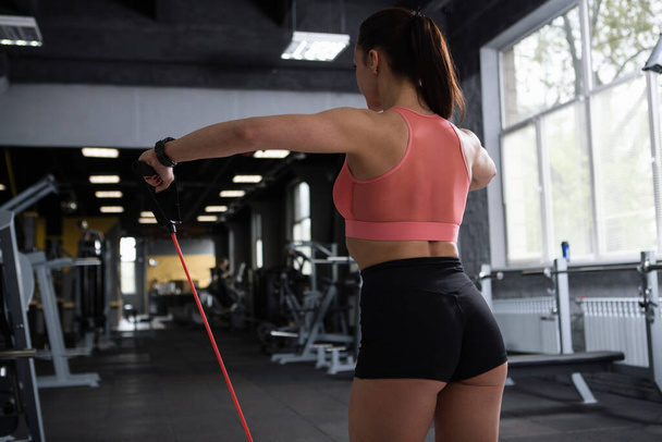 Atletická nepoznatelná žena cvičí s páskou odporu v tělocvičně, zadní pohled záběr - Fotografie, Obrázek