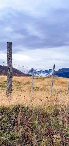 A vertical shot of barbed wire fence with beautiful snow-capped mountains in the background - Foto, Bild