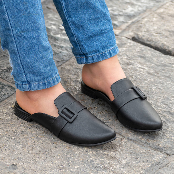 Closeup of a person wearing stylish and beautiful black colored leather mule shoes - Foto, Imagen