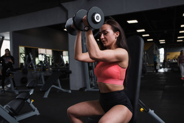 Güçlü kolları olan genç sporcu kadın spor salonunda halterlerle egzersiz yapıyor, boşluğu kopyalıyor. - Fotoğraf, Görsel