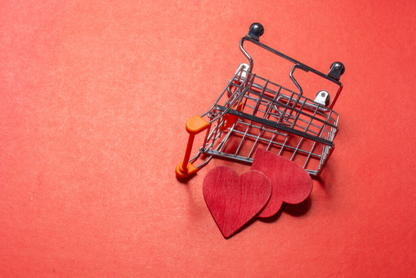 A miniature shopping cart with paper hearts on red background - Photo, Image