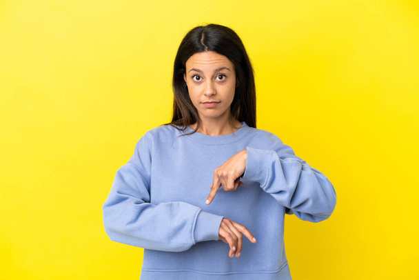 Young caucasian woman isolated on yellow background making the gesture of being late - Φωτογραφία, εικόνα
