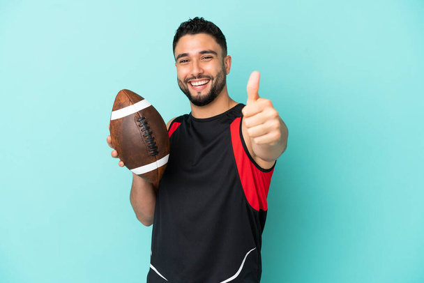 Young arab man playing rugby isolated on blue background with thumbs up because something good has happened - Fotografie, Obrázek