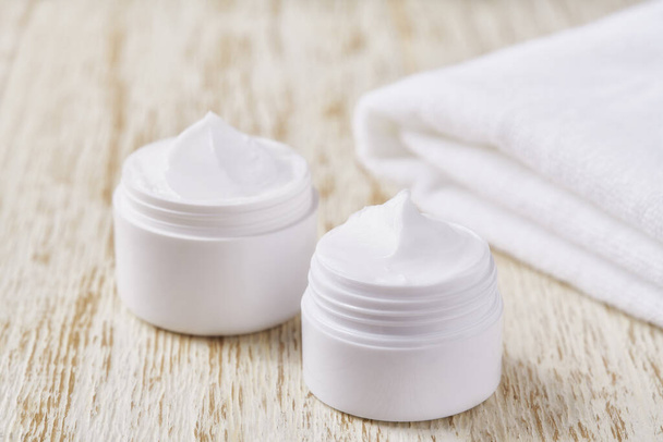 Hygiënische crème huidverzorgingsproduct in plastic pot met handdoek op witte tafel. - Foto, afbeelding