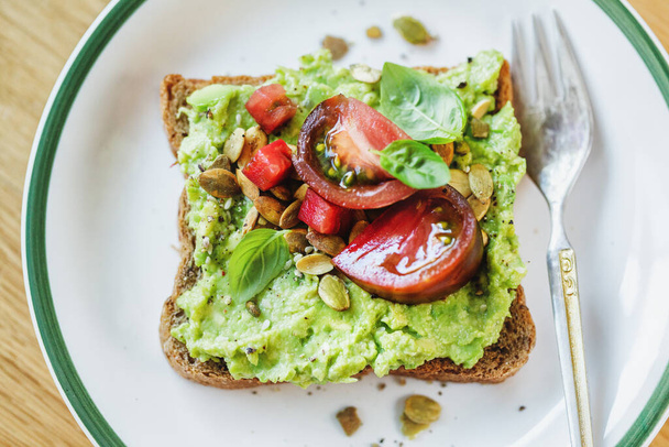 Tasty sandwich on wholegrain bread with mashed avocado and tomatoes. Closeup.  - Foto, Imagem
