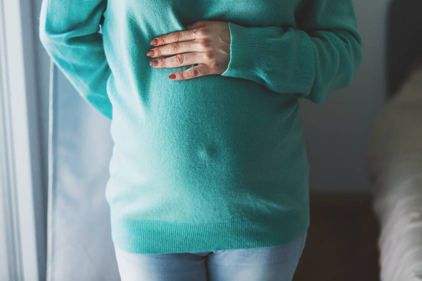 Pregnant woman touching belly in sweater being home enjoying pregnancy. Lifestyle. Maternity concept.  - 写真・画像