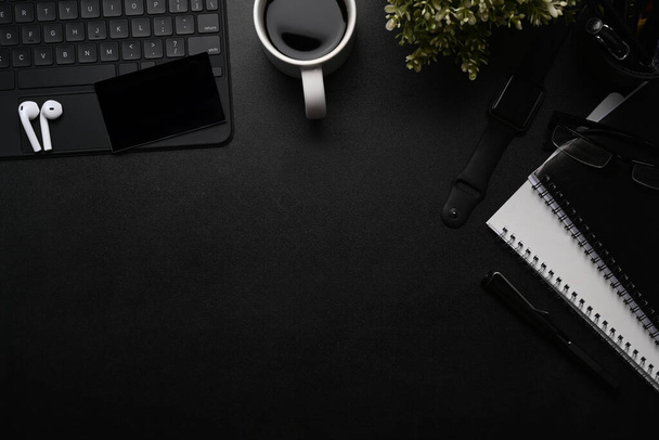 Overhead shot of dark office desk with wireless earphone, smart watch, notebook, wireless keyboard and copy space. - Photo, Image