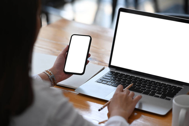 Zadní pohled na podnikatelku pracující s počítačem notebookem a pomocí mobilního telefonu v moderní kanceláři. - Fotografie, Obrázek