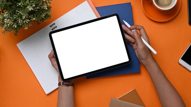 Overhead-Aufnahme einer jungen Designerin mit digitalem Tablet und Stift auf orangefarbenem Hintergrund. - Foto, Bild