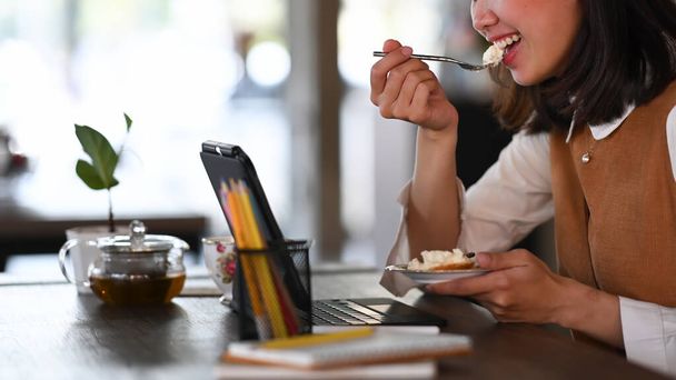 Cortado tiro de mujer que trabaja con la tableta del ordenador y comer postre en la cafetería. - Foto, imagen