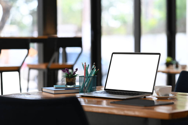Ordenador portátil con pantalla en blanco, taza de café anuncio suministros de oficina en escritorio de oficina de madera. - Foto, imagen