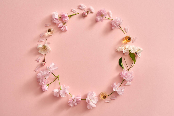 Spring concept with bottles of essential oil with fresh pink kwanzan cherry flowers on pastel pink background, with copy space - Foto, Imagem