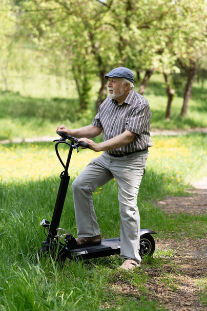 前向きな老人が公園へ散歩に行き、停車し、隣に電動スクーターが立っていた。夏、晴れた日。高齢者の健康的なライフスタイル. - 写真・画像