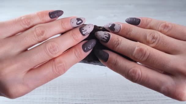 Kobiece dłonie z pięknymi paznokciami manicure w postaci czekoladowych cukierków, łamiąc rozłożony batonik ciemnej czekolady, zbliżenie. Smacznego.. - Materiał filmowy, wideo