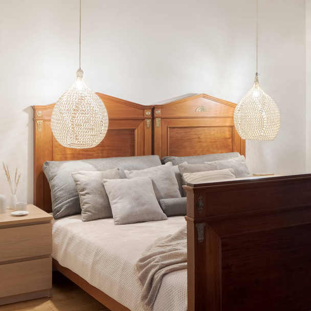 Cama elegante, de madera y estilo anticuado para dos personas en un dormitorio sencillo con mesita de noche de madera y dos lámparas colgantes de ratán - Foto, Imagen