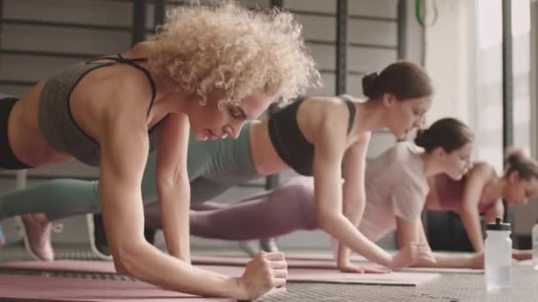 昼間のフィットネスルームでヨガマットの上の板の位置で肘と上にまっすぐ腕に降りて4つのリーンスポーツ女性のロックダウン - 映像、動画