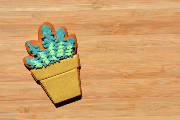 Gingerbread cookie decorated with icing in the shape of a potted plant isolated on a wood background with copy space. - Foto, afbeelding