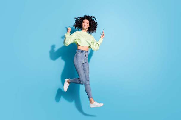 Full length photo of delighted person fist up celebrate jump high beaming smile isolated on blue color background - Fotó, kép
