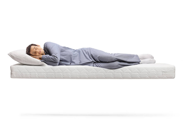 Full length shot of a man in pajamas sleeping peacefully on a floating mattress isolated on white background - Фото, зображення