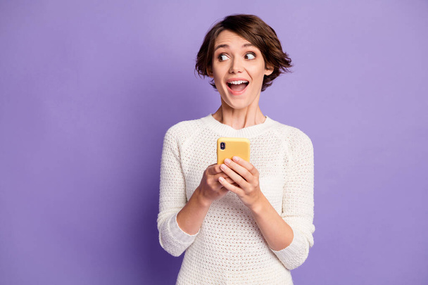 Photo portrait of curious surprised female student keeping cellphone looking at blank space isolated on vivid purple color background - Foto, Bild