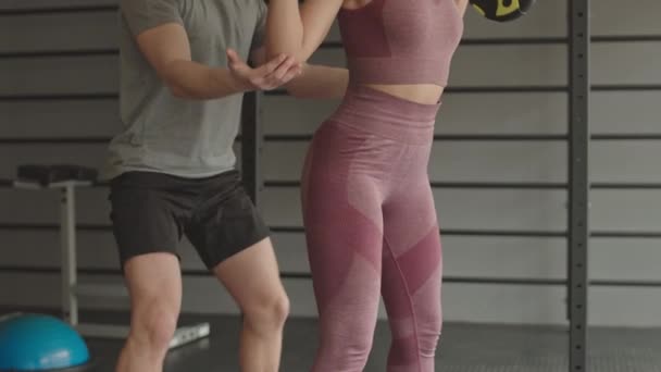 Opsluiting van jonge Mixed-Race vrouwelijke atleet dragen leggings en gewas top, squats doen met lange halter, jonge mannelijke coach verzekeren haar - Video