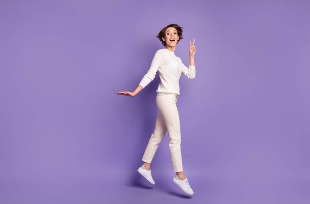 Full length body size photo of cheerful girl jumping showing peace v-sign gesture isolated on pastel purple color background - Zdjęcie, obraz