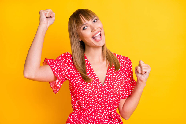 Photo of adorable lucky young lady wear red clothes rising fists isolated yellow color background - Φωτογραφία, εικόνα