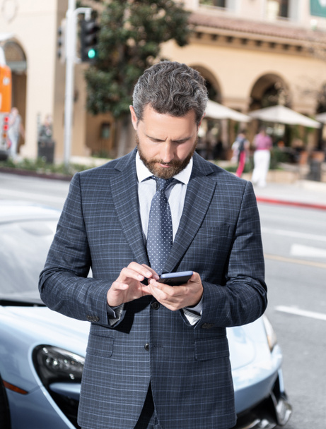 handsome mature man businessman in businesslike suit stand by luxury car outdoor and chatting on phone, communication. - Photo, Image