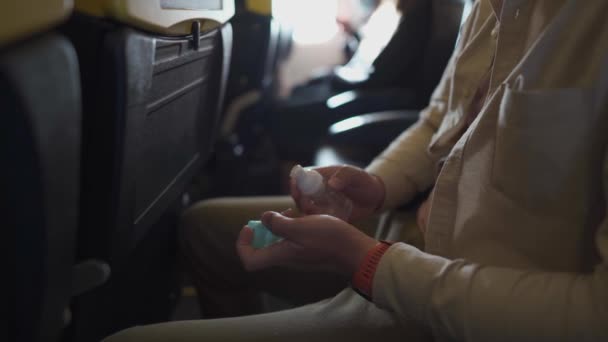 Ręczne nagranie mężczyzny noszącego osłonę przeciwpożarową na pokładzie samolotu. Mężczyzna w masce ochronnej używa żelu nasączonego alkoholem, dezynfekuje dłonie w samolocie, chroni covid-19, nowa koncepcja normalnego podróżowania - Materiał filmowy, wideo