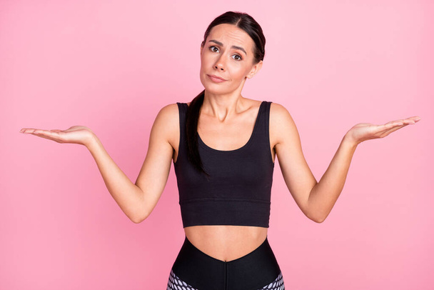 Photo of clueless young brunette woman shrug shoulders hold hands empty space scales isolated on pink color background - Foto, immagini