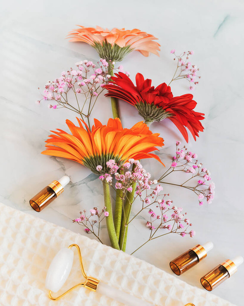 Home skin care and spa relax concept. Romantic, wellness, cosmetic composition with bouquet of gerberas, bottles of serum and oils and cosmetics accessories on a light background - Foto, afbeelding