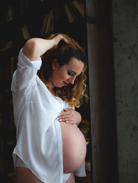 boldog terhes nő ölelgeti a hasát a kezével és nézi. - Fotó, kép