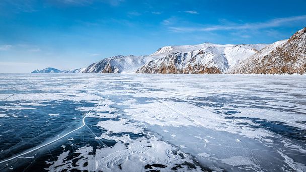 Long, sinuous cracks extend beyond the horizon on the dark, endless ice of Lake Baikal - Photo, Image