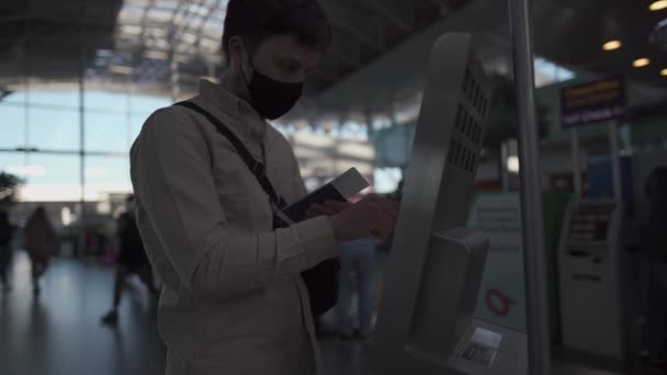 Man met gezichtsmasker aan boord op de vlucht op de luchthaven. Reizigers typen op het touchscreen van het zelfincheckstation in de terminal. Vluchtregistratie, coronavirus uitbraak. Zelfbedieningsmachine bij vertrek - Video
