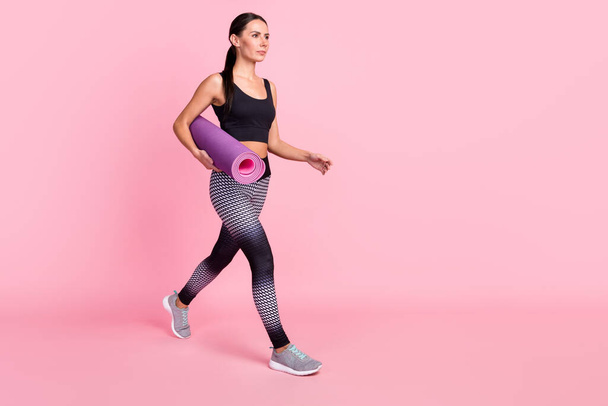 Photo of pretty charming young lady sportswear running fast holding yoga mat looking empty space isolated pink color background - Fotografie, Obrázek