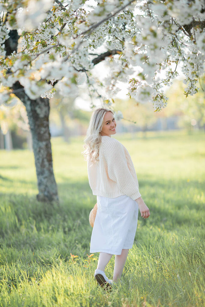 Όμορφη νεαρή γυναίκα ξεκουράζεται σε ένα πικνίκ σε έναν ανθισμένο κήπο. Λευκά λουλούδια. Άνοιξη. - Φωτογραφία, εικόνα