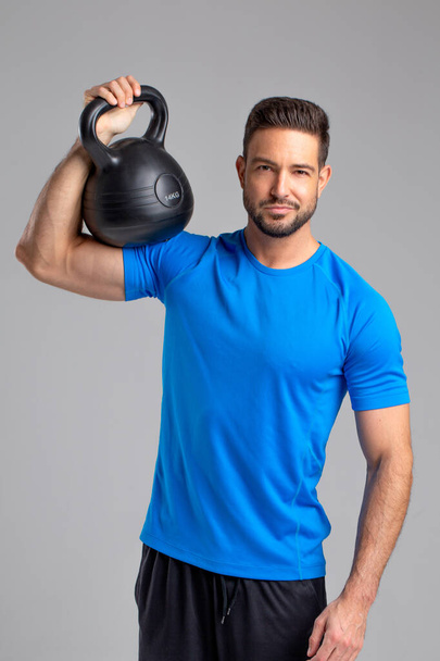Young sporty fit 30s caucasian man posing with kettlebell on grey background - Fotó, kép